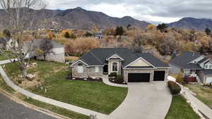 View of front of house with a mountain view, an attached garage, concrete driveway, a front yard, and stone siding