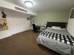 Carpeted bedroom featuring a textured ceiling, a desk, and a closet