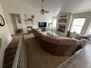 Carpeted living room featuring a tiled fireplace, a ceiling fan, lofted ceiling, and a textured ceiling