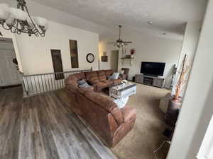Living room with a chandelier, a textured ceiling, vaulted ceiling, ceiling fan, and wood finished floors