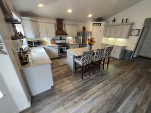 Kitchen with a breakfast bar, a kitchen island, stainless steel appliances, custom exhaust hood, and dark wood-style floors