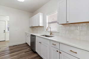 Kitchen featuring white cabinetry, backsplash, dark wood finished floors, dishwasher, and light stone countertops