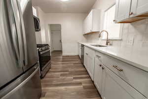 Kitchen featuring appliances with stainless steel finishes, white cabinets, dark wood-type flooring, light stone counters, and a textured ceiling
