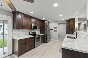 Kitchen with appliances with stainless steel finishes, backsplash, dark brown cabinets, light wood-type flooring, and recessed lighting