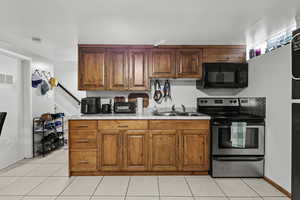 Kitchen featuring electric stove, light countertops, black microwave, light tile patterned floors, and brown cabinetry