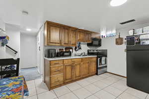 Kitchen featuring black appliances, light countertops, brown cabinetry, and light tile patterned flooring