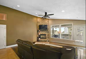 Living area featuring a textured ceiling, lofted ceiling, a fireplace, ceiling fan, and recessed lighting