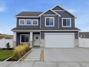 Craftsman inspired home featuring stone siding, driveway, a garage, a gate, and a shingled roof