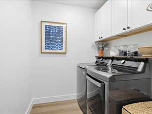 Laundry area with light wood-style flooring, washing machine and dryer, and cabinet space