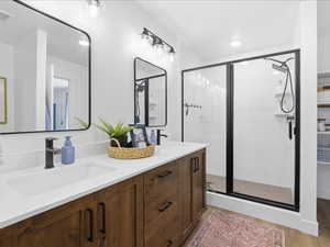 Full bath with double vanity, a stall shower, and light wood-style floors