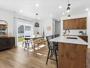 Kitchen with hanging light fixtures, light wood finished floors, recessed lighting, brown cabinetry, and a breakfast bar area