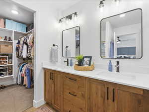 Ensuite bathroom featuring double vanity, a spacious closet, recessed lighting, and ceiling fan