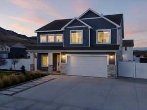 Craftsman house with stone siding, concrete driveway, covered porch, a garage, and a gate
