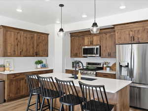 Kitchen with appliances with stainless steel finishes, a breakfast bar, a center island with sink, light wood-type flooring, and pendant lighting