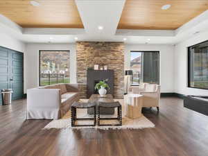 Living area with a raised ceiling, wood ceiling, wood finished floors, a stone fireplace, and recessed lighting