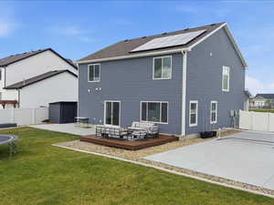 Back of house with a fenced backyard, a trampoline, a wooden deck, roof mounted solar panels, and outdoor lounge area