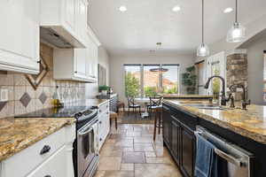 Kitchen featuring appliances with stainless steel finishes, hanging light fixtures, recessed lighting, light stone countertops, and stone tile floors