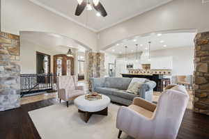 Living room featuring arched walkways, ornamental molding, dark wood-style floors, ceiling fan, and decorative columns