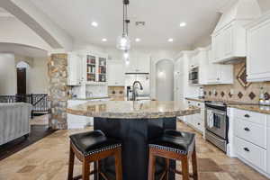 Kitchen featuring arched walkways, a center island with sink, appliances with stainless steel finishes, decorative light fixtures, and decorative backsplash