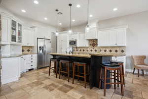 Kitchen featuring stainless steel appliances, a breakfast bar, pendant lighting, glass insert cabinets, and recessed lighting