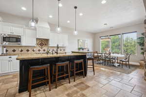 Kitchen with hanging light fixtures, white cabinetry, a breakfast bar area, decorative backsplash, and light stone counters