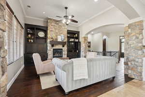 Living area with arched walkways, crown molding, a fireplace, dark wood-style flooring, and ceiling fan