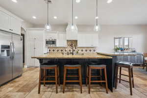 Kitchen with decorative light fixtures, stainless steel appliances, a breakfast bar area, white cabinetry, and decorative backsplash