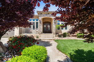 View of front of property with stone siding, a front yard, stucco siding, a tile roof, and french doors