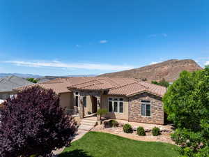 Mediterranean / spanish house with stone siding, stucco siding, a front yard, a mountain view, and a tile roof