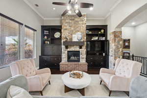 Living room with ornamental molding, a stone fireplace, ceiling fan, and wood finished floors