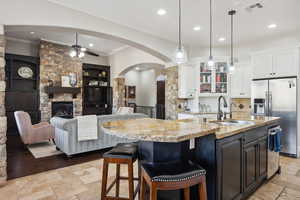 Kitchen featuring arched walkways, a stone fireplace, a breakfast bar, open floor plan, and appliances with stainless steel finishes