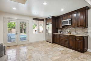 Kitchen featuring dark brown cabinets, french doors, appliances with stainless steel finishes, recessed lighting, and light stone countertops