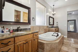 Bathroom with two vanities, a bath, stone tile floors, a ceiling fan, and recessed lighting