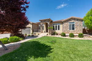 Mediterranean / spanish home featuring stone siding, a front yard, stucco siding, a tile roof, and an attached garage