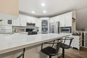 Kitchen with a kitchen breakfast bar, a peninsula, backsplash, white cabinets, and stainless steel appliances