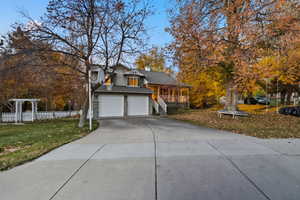 View of front facade with concrete driveway, a garage, a shingled roof, a chimney, and covered porch