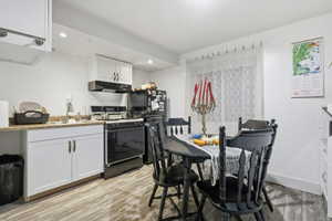 Kitchen featuring white cabinets, black appliances, light wood-style floors, under cabinet range hood, and recessed lighting