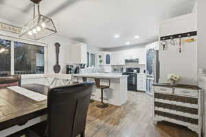 Kitchen with white cabinets, dark wood-style flooring, black stove, backsplash, and a breakfast bar area