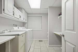 Laundry area featuring a paneled ceiling, light tile patterned flooring, washer and clothes dryer, and cabinet space