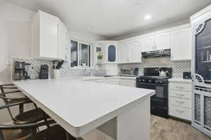 Kitchen with a peninsula, black gas stove, white cabinetry, light countertops, and a kitchen breakfast bar