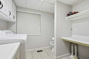 Washroom with a drop ceiling, light tile patterned floors, washing machine and clothes dryer, and cabinet space