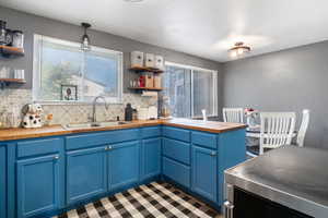 Kitchen with blue cabinets, backsplash, butcher block countertops, open shelves, and range with electric cooktop