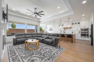 Living room with a tray ceiling, light wood finished floors, recessed lighting, and a ceiling fan