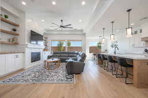 Living room with light wood-style floors, a glass covered fireplace, recessed lighting, and ceiling fan