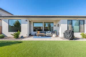 Rear view of house with stucco siding, a lawn, and a patio