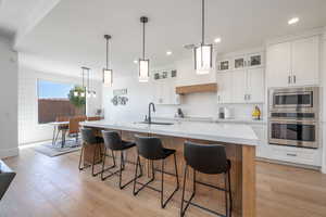 Kitchen featuring glass insert cabinets, appliances with stainless steel finishes, white cabinets, light wood-style flooring, and recessed lighting