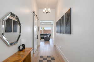 Corridor featuring light wood-style floors, a chandelier, and a barn door