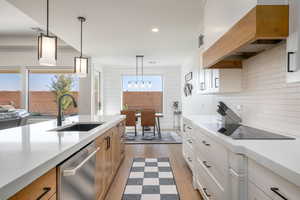 Kitchen with white cabinetry, light wood-type flooring, light stone counters, pendant lighting, and stainless steel dishwasher