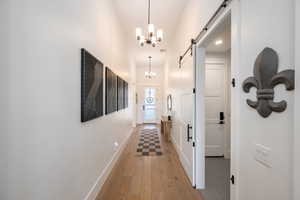 Hall featuring a barn door, a chandelier, and light wood-style flooring