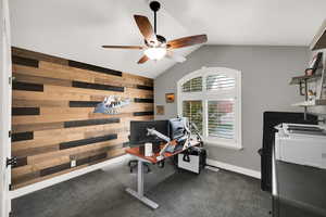 Office featuring lofted ceiling, a ceiling fan, wood walls, and dark colored carpet